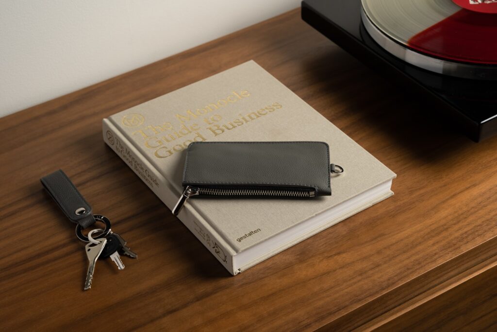 Photo of a gray leather zip wallet and key organizer on a wooden table next to a vinyl record player.