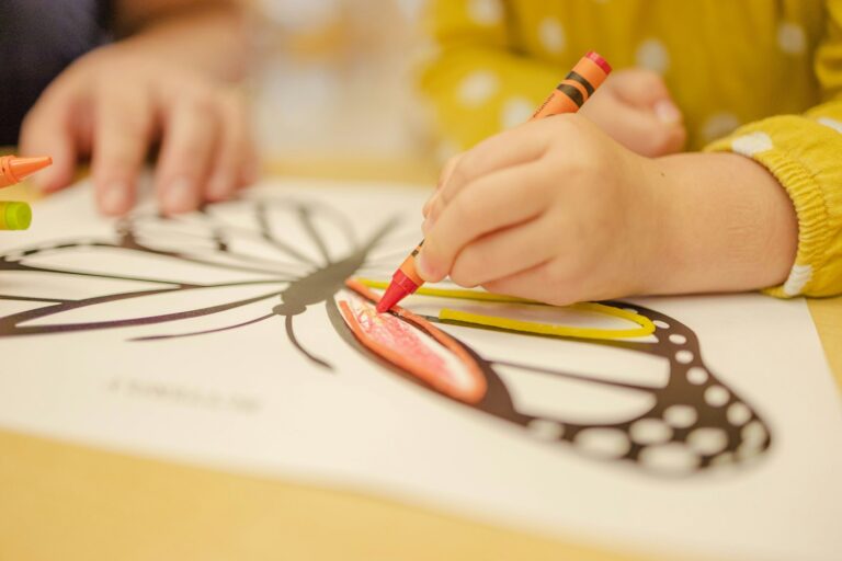 Enfant en pull jaune qui colorie un papillon au crayon de cire sur une planche imprimée